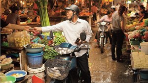 VIETNAM, Hanoi, Chau Long Market, a man rides him moped through the market and stops to buy some potatoes